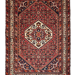 Full view of a 4' 11" x 6' 1" hand-knotted Persian Hamedan wool rug featuring a central geometric medallion on a vibrant madder red field.