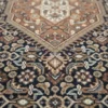 Macro shot of the central tan diamond medallion and the intricate navy Herati pattern on a hand-knotted Bijar rug.