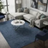 Modern living room with a grey sectional sofa and marble coffee table, featuring a 5'3" x 7'1" blue Indian Gabbeh rug on dark wood floors.