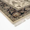 Detailed corner view of an ivory Indian wool rug showing the ornate navy blue floral border and clean white hand-bound fringe.