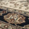 Macro shot of the dense hand-knotted wool pile and detailed floral patterns in tan, brown, and sage green on an ivory background.
