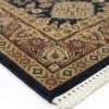 Detailed corner view of a navy Indian wool rug showing the wide floral border and clean white hand-bound fringe.