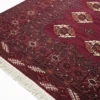Detailed corner view of a burgundy Turkmen rug showing the intricate geometric border and clean white fringe on a white background.