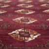 Macro shot showing the dense hand-knotted wool pile and intricate geometric Gul medallions on a burgundy Turkmen rug.