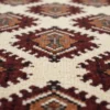 Macro shot showing the dense hand-knotted wool pile and detailed geometric Gul medallions in burgundy, orange, and charcoal on an ivory rug.