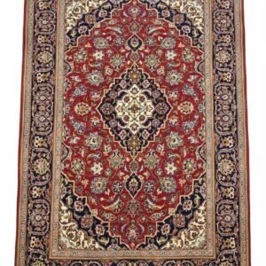 Full overhead view of a rectangular hand-knotted Persian Kashan wool rug featuring a red field with a central ivory diamond medallion and an ornate navy blue border.