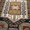 Close-up of the hand-knotted wool pile showing a central white geometric medallion with yellow and green accents on a Kazak rug.