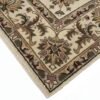 Detailed corner view of a cream and tan botanical Indian rug showing the ornate border and clean white fringe.