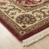 Detailed corner view of a red and cream Indian rug showing the clean edges and short cream fringe on a light wood floor.