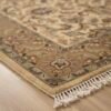 Detailed corner view of a floral Indian rug showing the tan border patterns and white fringe on a light wood floor.
