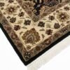 Detailed corner view of a black and cream Indian rug showing the ornate border patterns and clean white fringe.