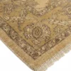 Detailed corner view of a tan Afghan Chobi rug showing the wide floral border and short hand-bound wool fringe.