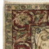 Detailed corner view of a burgundy Indian wool rug showing the ornate ivory and navy border patterns and clean white hand-bound fringe.