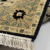 Detailed corner view of a navy Indian wool rug showing the wide ivory floral border and hand-bound fringe.
