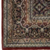 Detailed corner view of a burgundy Indian wool rug showing the wide cream floral border and clean white hand-bound fringe.