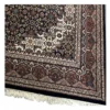 Detailed corner view of a navy Indian wool rug showing the ornate ivory floral border and clean white hand-bound fringe.