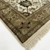 Detailed corner view of a navy Indian rug showing the ornate ivory floral border and hand-bound fringe.