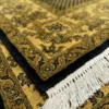 Detailed corner view of a black Indian wool rug showing the wide ornate gold border and clean white hand-bound fringe.