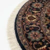 Detailed edge view of a circular Indian rug showing the ornate navy floral border and authentic white hand-bound fringe.