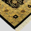 Detailed corner view of a black Indian wool rug showing the wide ornate gold border and clean white hand-bound fringe.