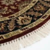 Detailed edge view of a circular Indian rug showing the ornate navy border, gold vine work, and authentic white hand-bound fringe.