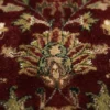 Macro shot of the dense hand-knotted wool pile showing detailed floral vine patterns in gold, sage green, and navy on a red background.
