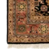 Detailed corner view of a black Indo wool rug showing the wide ornate terracotta border and clean white hand-bound fringe.