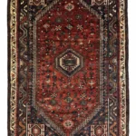 Full overhead view of a rectangular 5' 11" x 8' hand-knotted Persian Qashqai wool rug with a rich red field and three central navy geometric medallions.