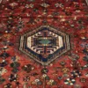 Macro shot of the central navy hexagonal medallion and the dense hand-knotted wool pile on a red Persian Qashqai rug.