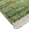 Detailed corner view of a forest-green Persian Gabbeh rug showing the sturdy hand-bound edges and thick, cream-colored wool fringe.