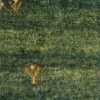 Macro shot of the thick, plush hand-knotted wool pile on a green Persian Gabbeh rug, highlighting the dense texture and natural color variations.