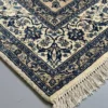 Detailed corner view of a sand-colored Persian Lori rug showing the wide navy floral border and hand-bound fringe.