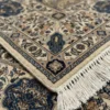 Detailed corner view of a Nain wool rug showing the ornate ivory and blue floral border and clean white hand-bound fringe.