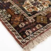 Detailed corner view of a red Persian Qashqai rug showing the multi-layered geometric border and authentic hand-bound wool fringe.