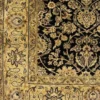 Macro shot of the dense hand-knotted wool pile showing intricate sage green and golden floral motifs on a deep black background.