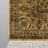 Detailed corner view of an olive-gold Indian rug showing the ornate botanical border and clean white hand-bound fringe.