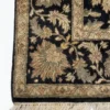 Detailed corner view of a black Indian rug showing the ornate sage-green floral border and clean white hand-bound fringe.
