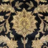 Macro shot of the dense hand-knotted wool pile showing an oversized sage green and gold floral motif on a black background.
