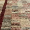 Macro shot of the thick hand-knotted wool pile on a burgundy Afghan Gabbeh rug, showing the textured grid pattern and soft color variations.