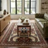 A bright living room with large windows, featuring a tufted green leather sofa and a glass coffee table set atop an Afghan Kazak wool rug.