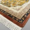 Detailed corner view of a gold Chinese rug showing the ornate terracotta and black border system and clean white hand-bound fringe.