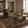 Sophisticated living room with a moss green armchair and wooden table, featuring a red, beige, and black Indian wool rug.