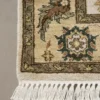 Detailed corner view of a black Indian rug showing the wide ornate gold-tan botanical border and clean white hand-bound fringe.