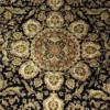 Macro shot of the central medallion on a black Indian wool rug showing dense hand-knotted floral details in rust, cream, and olive green.