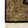 Detailed corner view of a black Indian rug showing the ornate terracotta botanical border and clean white hand-bound fringe.