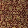 Macro shot of the dense hand-knotted wool pile showing intricate gold and tan floral motifs on a deep red background.
