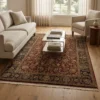 Elegant living room with neutral sofas and a glass coffee table, featuring a 5' 9" x 8' 8" red, gold, and black Indian wool rug as a central anchor.