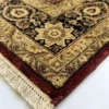 Detailed corner view of a red Indian rug showing the ornate gold-tan botanical border and clean white hand-bound fringe.