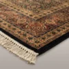 Detailed corner view of an olive-gold Indian rug showing the ornate botanical border and clean white hand-bound fringe.