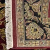 Close-up view of the underside of a square crimson Indian wool rug, showing individual hand-tied knots and authentic textile construction.